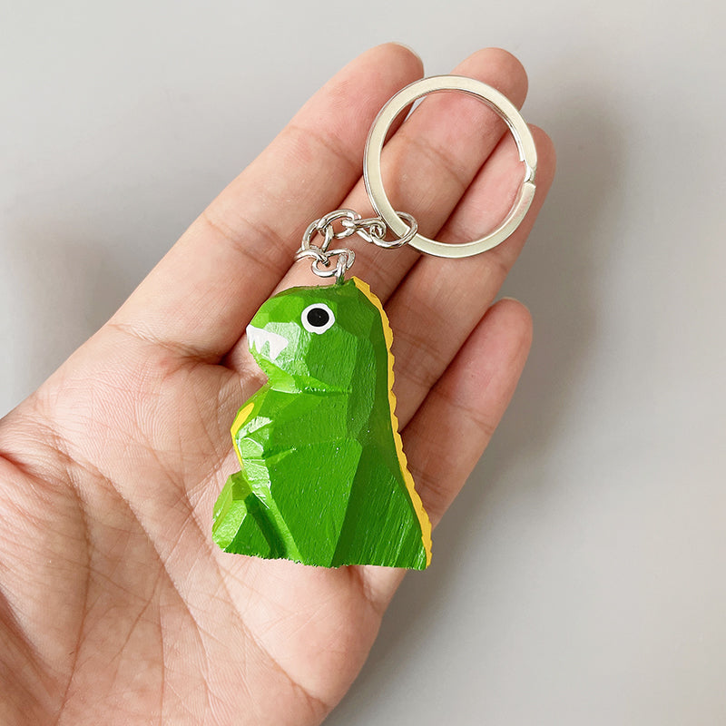 Hand-painted dinosaur keychain with white teeth and big eyes, held in an open hand, perfect for backpacks or as a unique small gift.