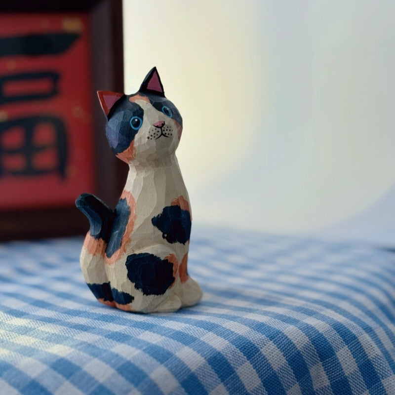 Hand-carved wooden calico cat figurine in seated position with upward gaze