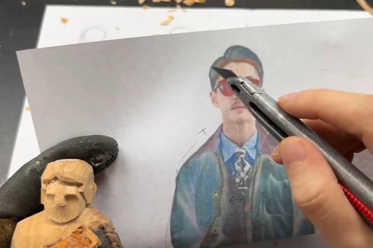 Comparing a wooden gift figure with a reference photo to analyze hairstyle proportions before carving.