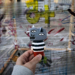 Guernica-style hand-carved figure held in front of a wall covered in colorful graffiti.