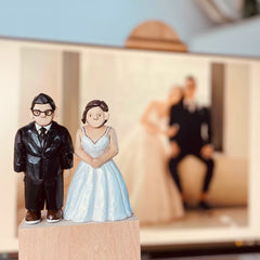 Custom figurine of a bride and groom in wedding attire, hand-carved and displayed with their wedding photo in the background.