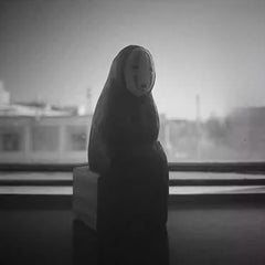 No Face Figure sculpture in silhouette near a window with blurred city background.