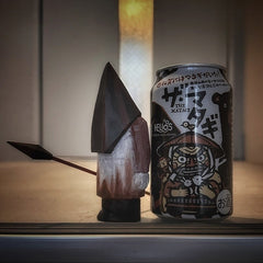 Pyramid Head wooden statue standing next to a Japanese beer can, showing scale and handmade texture.