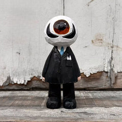 Hand carved wooden eyeball figure in black suit displayed against a wooden wall
