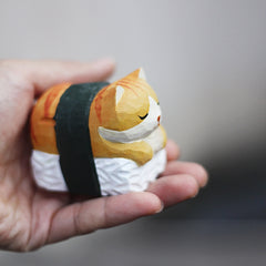 Sushi sleeping cat figurine is held in the hand, showing small and delicate.
