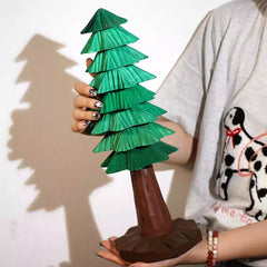 Tall wooden Christmas tree wood carving held by hand, showcasing layered green branches and natural trunk design.