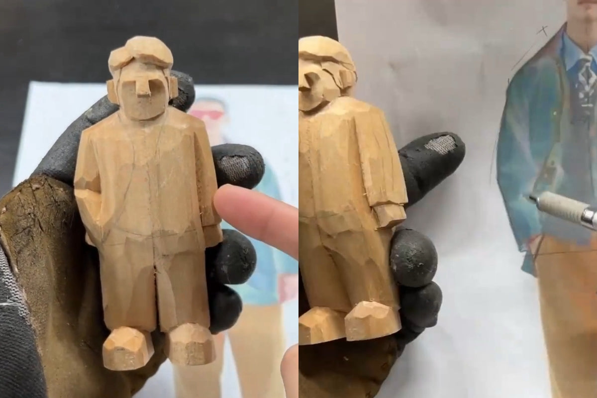 Close-up of a gloved hand holding a partially carved wooden figurine, showing early detailing of clothing lines.
