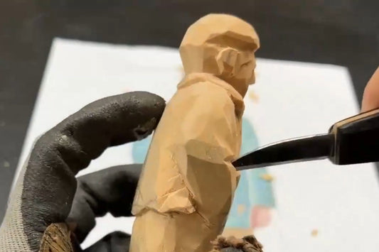 Close‑up of carving a wooden figurine, showing the knife shaping the sleeve and clothing folds — a detailed wood carving figures process for creating handcrafted Svn Futures  gifts.